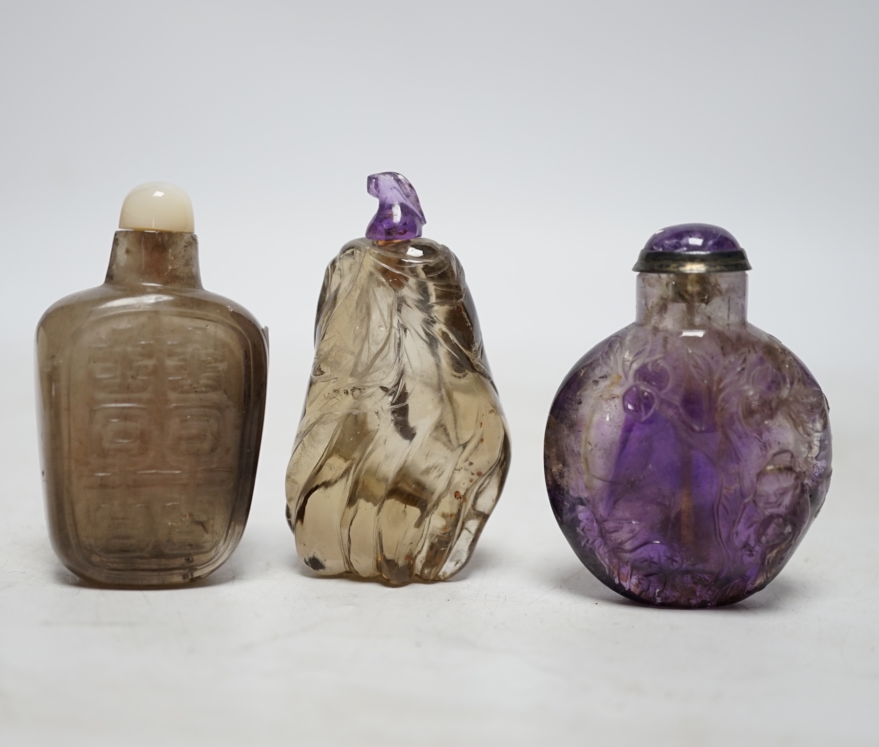 Three Chinese carved quartz snuff bottles, 19th/20th century to include a smoky quartz shuangxi bottle, an amethyst quartz bottle and a small smoky quartz gourd shaped bottle, largest 6.5cm high